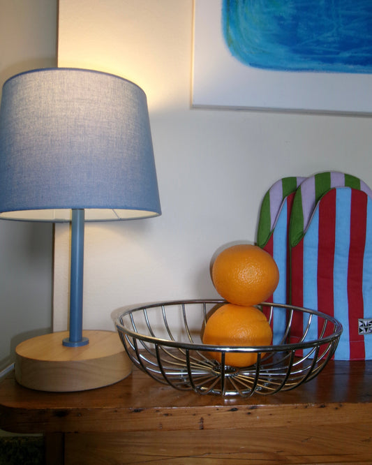2 oranges in a chrome bowl next to a blue lamp and striped pot holders in a colorful, playful kitchen