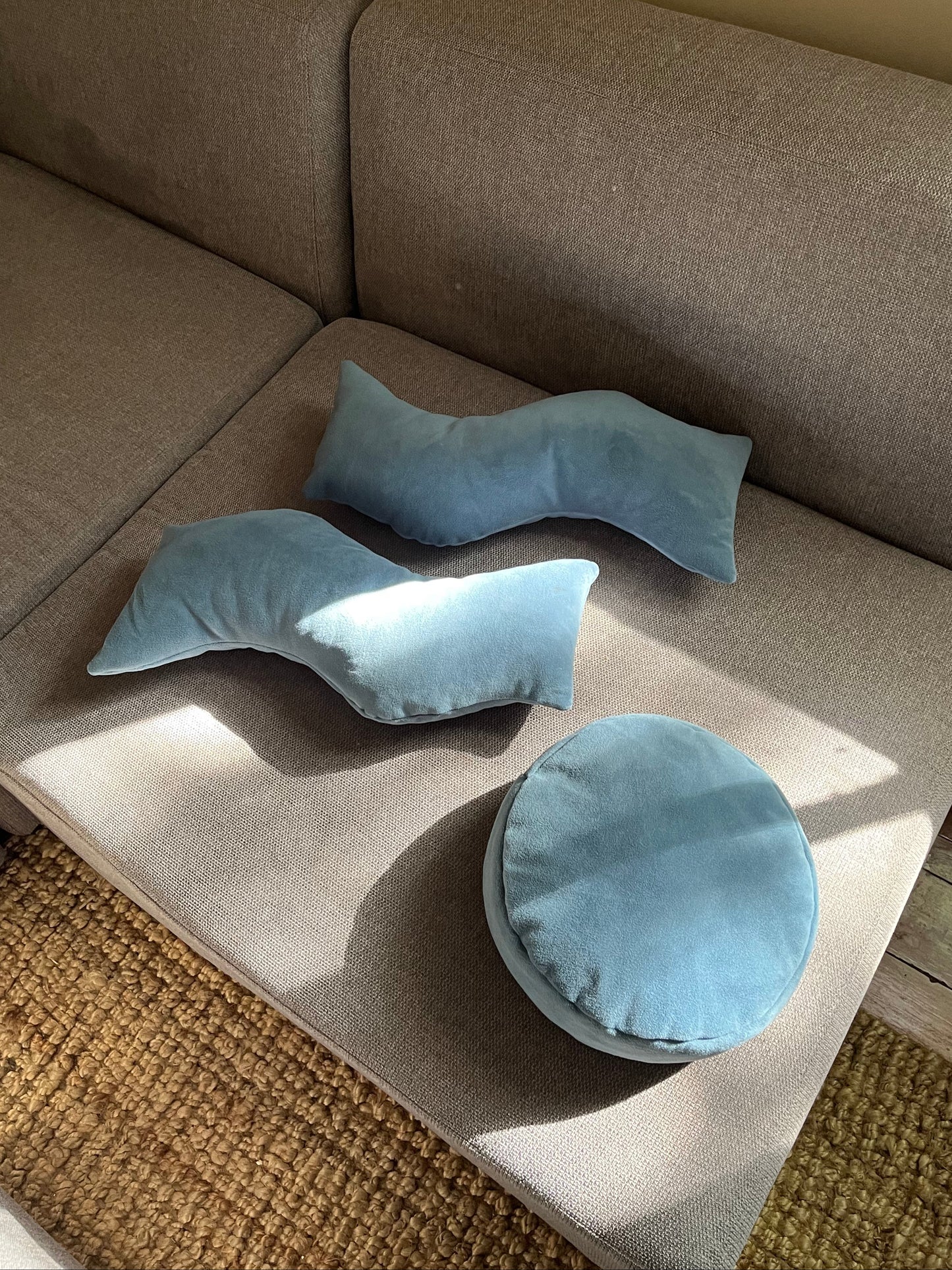 Two "This That" wavy pillows on a gray couch with another round pillow off to the side. Product Photography.
