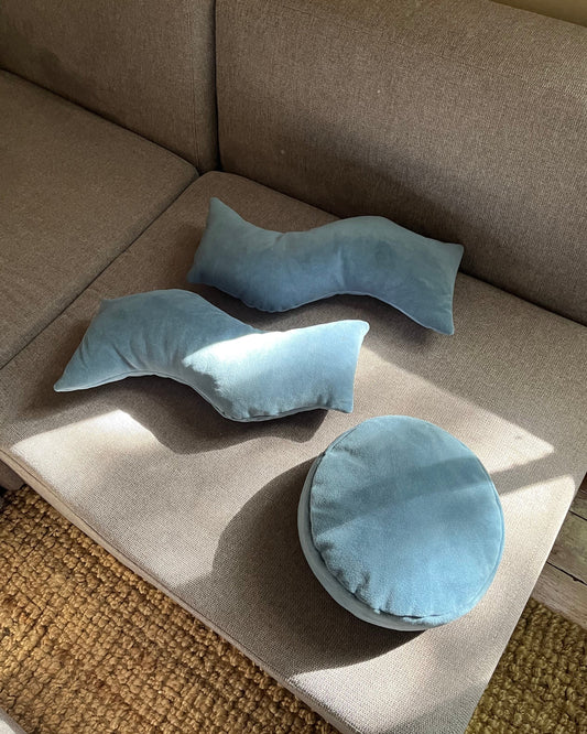 Two "This That" wavy pillows on a gray couch with another round pillow off to the side. Product Photography.