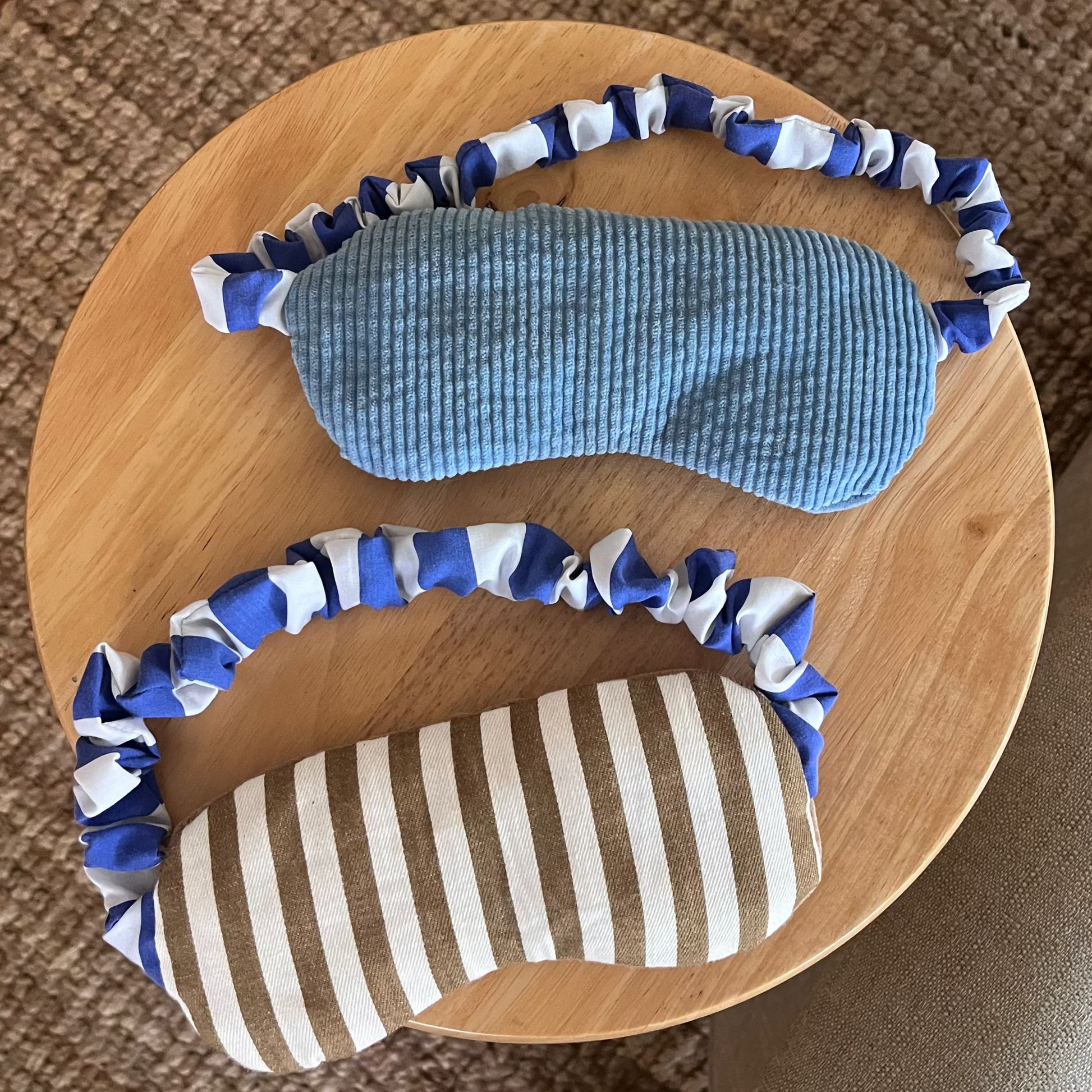Two eye masks with blue and white stripe elastic bands on a wooden surface.