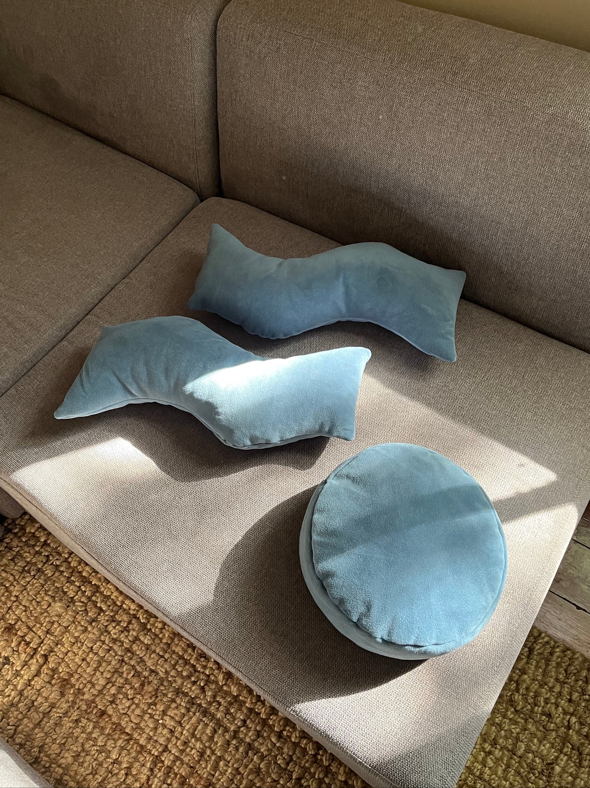 Two "This That" wavy pillows on a gray couch with another round pillow off to the side. Product Photography. 